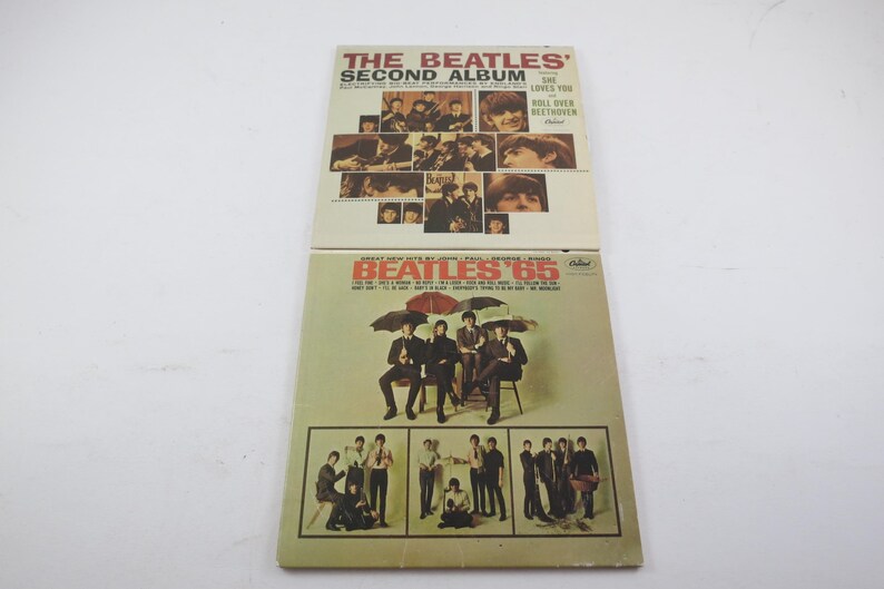 May include: Two vintage vinyl record albums. The top album is "The Beatles' Second Album" with images of the band. The bottom album is "Beatles '65" with the band under umbrellas and other images.