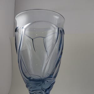 Pu&ograve; includere: Un bicchiere alto e trasparente blu con un design decorativo a spirale. Il bicchiere ha un'ampia bocca e un corpo strutturato e modellato. Il bicchiere viene probabilmente utilizzato per le bevande ed &egrave; posto su uno sfondo bianco.