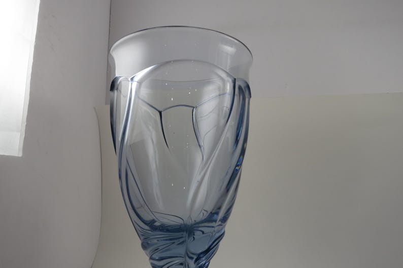 Pu&ograve; includere: Un bicchiere alto e trasparente blu con un design decorativo a spirale. Il bicchiere ha un'ampia bocca e un corpo strutturato e modellato. Il bicchiere viene probabilmente utilizzato per le bevande ed &egrave; posto su uno sfondo bianco.