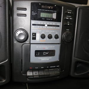 May include: Black Sony boombox with two speakers. The boombox has a digital display, a cassette player, and radio controls. The speakers have a mesh grill. The model number is CFD-Z110.