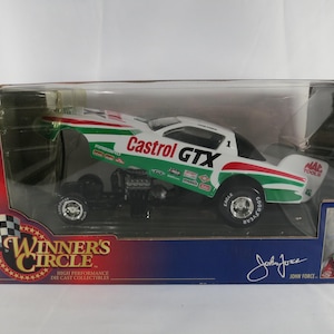 May include: A 1/24 scale Winner's Circle die-cast collectible funny car in a box. The white race car features green and red stripes, Castrol GTX branding, and the number 1. The packaging includes a photo of John Force and his signature.