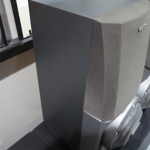 May include: A pair of gray Sony speakers. The speakers have a rectangular shape with a textured gray fabric on the top and a silver base. The front of the speakers have a metal mesh design.