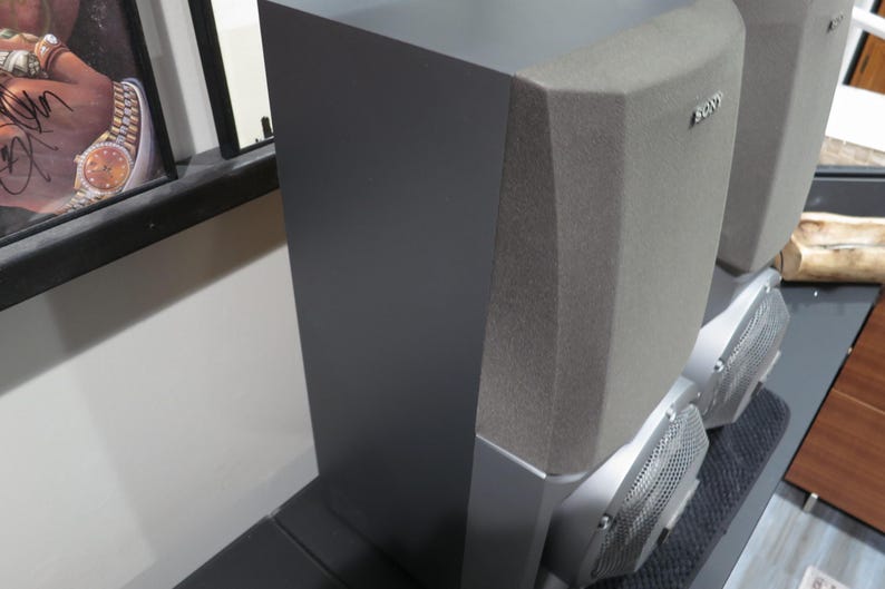 May include: A pair of gray Sony speakers. The speakers have a rectangular shape with a textured gray fabric on the top and a silver base. The front of the speakers have a metal mesh design.