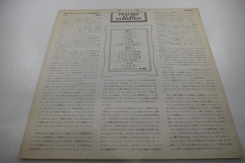 Puede incluir: Una portada de &aacute;lbum vintage con el t&iacute;tulo "Pictures at an Exhibition" en ingl&eacute;s. La portada presenta una lista enmarcada de piezas musicales y texto extenso en japon&eacute;s. El fondo es de color beige claro.