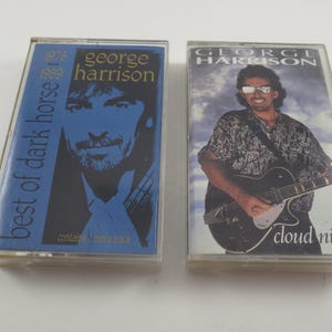 May include: Two cassette tapes featuring George Harrison. The first tape is blue and white and says "best of dark horse 1976-1989" and "George Harrison". The second tape is white and features a photo of George Harrison playing a guitar and says "George Harrison" and "Cloud Nine".