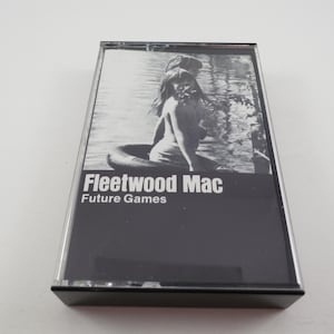 May include: A vintage cassette tape of Fleetwood Mac's album "Future Games." The album cover is black and white, featuring an image of a person in a tube on the water. The text "Fleetwood Mac" and "Future Games" are in white.