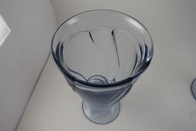 Pu&ograve; includere: Un calice di vetro trasparente tinto di blu, con un bordo ampio e decorativo e una base arrotondata. Il calice ha un design unico con linee curve e uno stelo. Il vetro &egrave; liscio e sembra essere fatto di un materiale resistente.