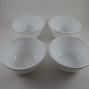 May include: Four white, round, ceramic bowls. The bowls are evenly spaced and have a simple, classic design. The bowls are suitable for serving soups, cereals, or other dishes. The bowls are clean and appear unused.