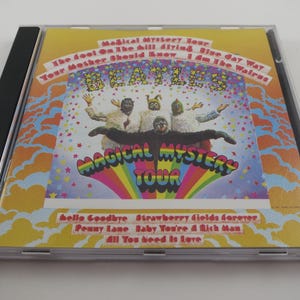 May include: A CD case featuring the album "Magical Mystery Tour" by The Beatles. The cover art is colorful, with the band members in costume. The album title is prominently displayed, along with song titles like "Hello Goodbye" and "Strawberry Fields Forever".