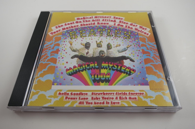 May include: A CD case featuring the album "Magical Mystery Tour" by The Beatles. The cover art is colorful, with the band members in costume. The album title is prominently displayed, along with song titles like "Hello Goodbye" and "Strawberry Fields Forever".