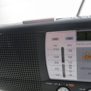 May include: Black Emerson radio with a digital clock and instant weather display. The radio has an AM/FM tuner, a telescoping antenna, and a speaker grill. The display shows the time and weather icons.