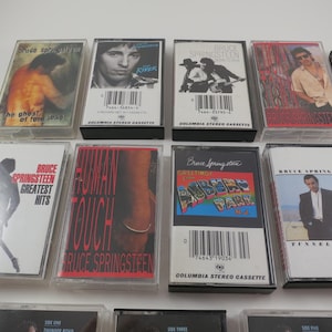 May include: A collection of vintage cassette tapes featuring album art from Bruce Springsteen. The tapes showcase various album covers with images of the artist and album titles. The collection includes titles like "Tunnel of Love" and "Human Touch".