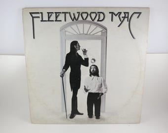 Puede incluir: Una portada de disco de vinilo cuadrada con el texto FLEETWOOD MAC en la parte superior. La imagen en blanco y negro muestra a una figura alta con traje oscuro y bastón junto a una figura más baja con camisa clara y pantalón oscuro.