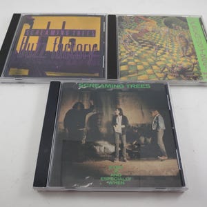 May include: Three compact disc cases featuring album art. The top two cases have colorful designs, while the bottom case features a black and white photo of three people. The text "Screaming Trees" is visible on all three cases.