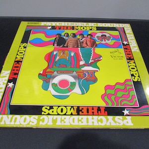 May include: A yellow vinyl record album cover with psychedelic artwork featuring a band of five men in front of a colorful, swirling design. The album title is "Psychedelic Sounds The Mops In Japan The Mops" and the record label is "Victor SJV-356".