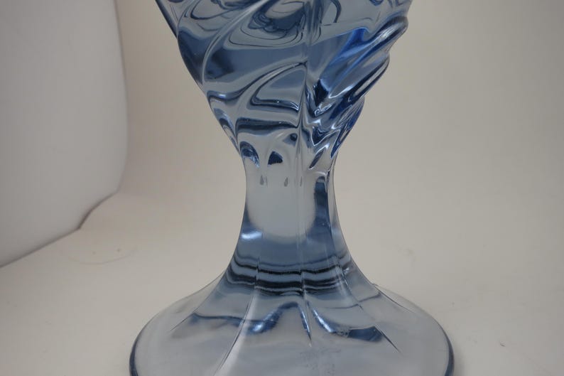 Pu&ograve; includere: Un vaso decorativo in vetro blu con un design a spirale e strutturato. Il vaso ha una base ampia che si assottiglia verso un collo stretto, per poi allargarsi di nuovo nella parte superiore. Il vetro ha una finitura lucida ed &egrave; traslucido.
