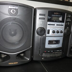 May include: A black and gray Sony CFD-210 boombox with two speakers. The boombox has a cassette player, radio, and CD player. The speakers have the words "Mega Bass" printed on them.