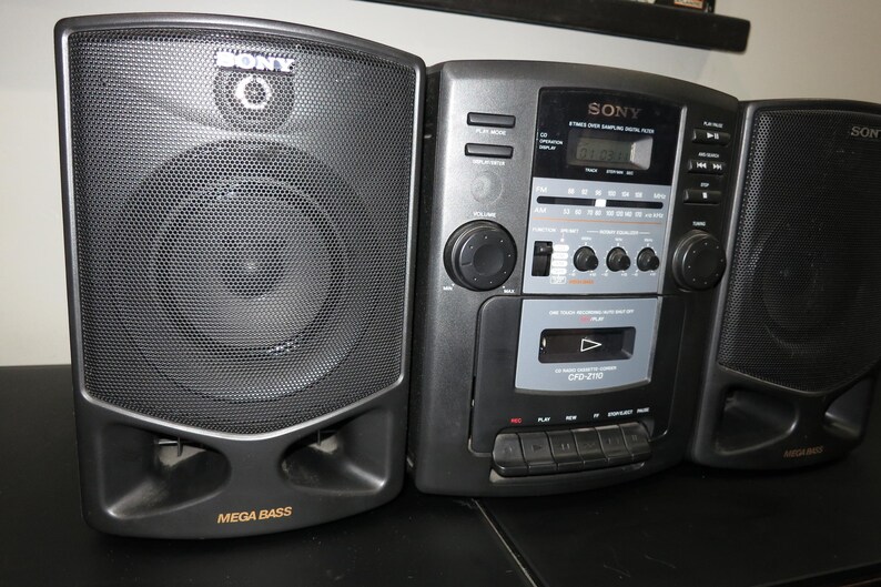 May include: A black and gray Sony CFD-210 boombox with two speakers. The boombox has a cassette player, radio, and CD player. The speakers have the words "Mega Bass" printed on them.