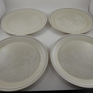 May include: Four oval-shaped cream-colored plates with a subtle, textured pattern. Each plate has a thin, dark blue border. The plates are arranged in a square formation, suitable for serving meals.