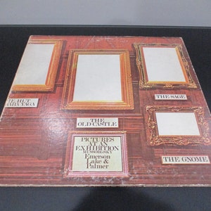 Op de afbeelding: Een vintage vinyl platenhoes met een bruine houten muur met vijf ingelijste foto's. Het album is getiteld "Pictures at an Exhibition" van Mussorgsky, Emerson Lake & Palmer. De titels van de foto's zijn "The Hut on Fowl's Legs", "The Old Castle", "The Sage" en "The Gnome".