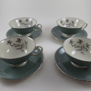 May include: Four vintage teacups and saucers. The cups and saucers are a muted teal color with a silver trim. The inside of the cups are cream-colored with a floral design. A classic set for tea parties or display.
