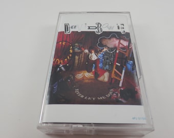 May include: A David Bowie cassette tape with the album art for "Never Let Me Down." The cover features a colorful, surreal illustration with a figure on a stage, a ladder, and the album title. The cassette is in a clear plastic case.