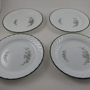 May include: Four white oval plates with a green floral design and a dark green rim. Two plates have a swirl pattern around the edge.