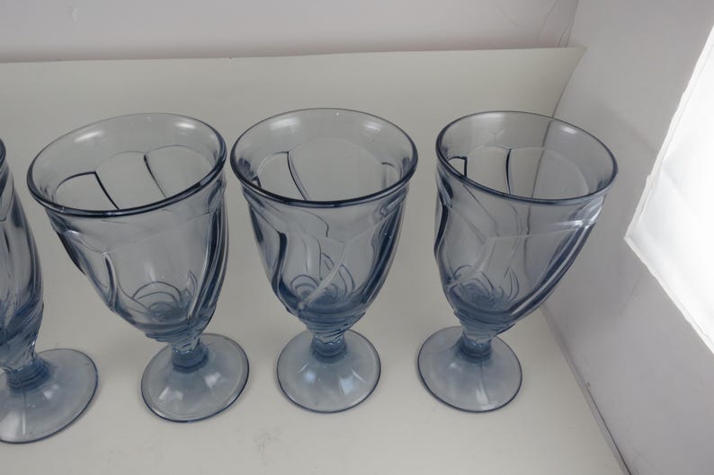 Pu&ograve; includere: Un set di quattro calici in vetro blu-tinto con un design decorativo a spirale. I calici hanno una forma a coppa arrotondata e poggiano su una base circolare. Le vetrerie sono adatte per servire bevande.