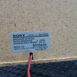 May include: Close-up of a speaker system component. A label with the "SONY" logo and model number "SS-W300" is affixed to a light brown wooden surface. The label includes technical specifications and a serial number.