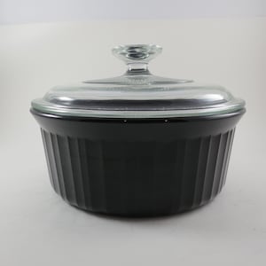 May include: A black, ribbed casserole dish with a clear glass lid. The lid has a clear glass knob. The dish is round and has a classic design. This is a kitchenware item.