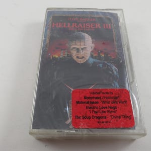May include: A clear plastic cassette case containing the Hellraiser III Hell on Earth movie soundtrack. The cover features Pinhead against a dark city background. A red sticker lists tracks by Motorhead, Material Issue, Electric Love Hogs, and The Soup Dragons.