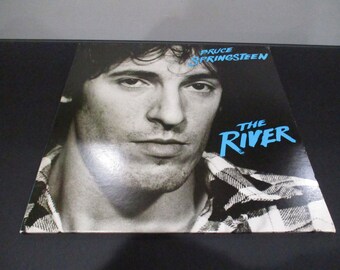 May include: A black and white photo of Bruce Springsteen on the cover of his album "The River". The album title is in blue text.