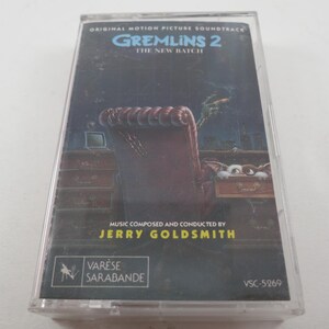 May include: A vintage cassette tape of the "Gremlins 2: The New Batch" original motion picture soundtrack. The cover art features a dark, detailed illustration of a chair and a Gremlin. The text includes the film title, composer Jerry Goldsmith, and the label Varese Sarabande.