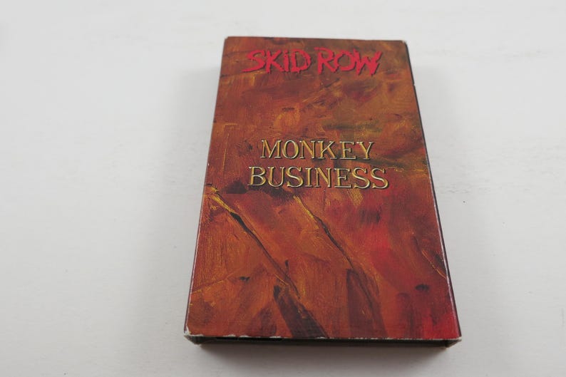 May include: A VHS cassette tape with an abstract design in shades of red, orange and yellow. The text "SKID ROW" and "MONKEY BUSINESS" is printed on the front of the tape.