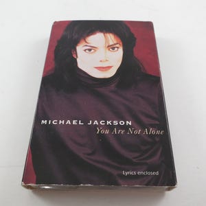May include: A CD case featuring Michael Jackson with the text "MICHAEL JACKSON You Are Not Alone" and "Lyrics enclosed". The image shows Jackson with dark hair and a dark turtleneck. The background is a dark red.