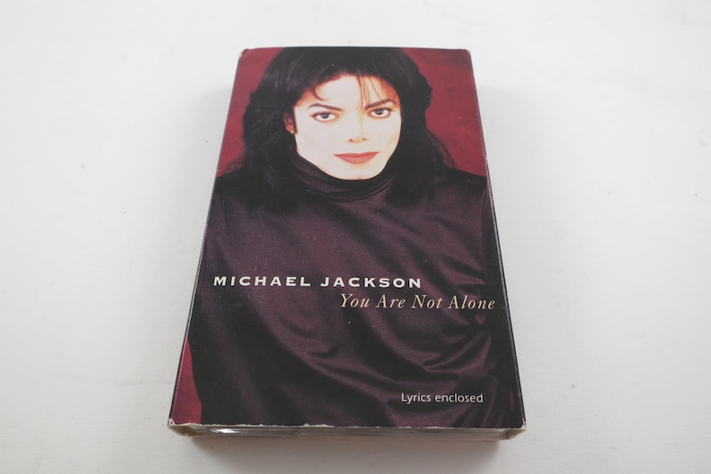 May include: A CD case featuring Michael Jackson with the text "MICHAEL JACKSON You Are Not Alone" and "Lyrics enclosed". The image shows Jackson with dark hair and a dark turtleneck. The background is a dark red.