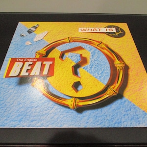 May include: A yellow and blue vinyl record with a gold circle and a question mark in the center. The text "The English Beat" and "What Is" are printed on the record.