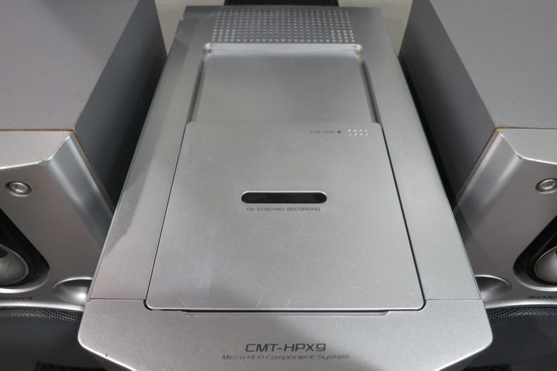 以下が含まれることがあります： CD SYNCHRO RECORDINGと記されたトップローディング式ディスクコンパートメントを備えた中央ユニットと、オーディオコンソールの両側に配置された2つのシルバーのスピーカーで構成される、シルバーのSony CMT-HPX9マイクロHi-Fiコンポーネントシステム。