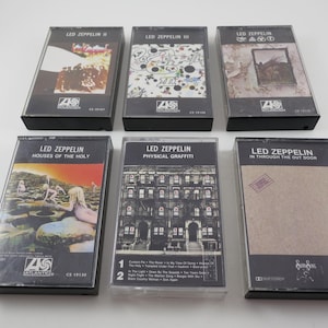 May include: Six Led Zeppelin cassette tapes. The album covers feature various designs, including a building facade, landscapes, and abstract art. The tapes are in black cases with the band's name and album titles visible.