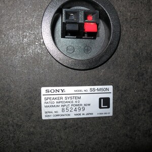 May include: The back panel of a black Sony SS-M50N speaker system featuring a circular terminal cup with one black and one red spring-clip connector. A white label displays technical specifications including 6 ohm impedance and 60W power.