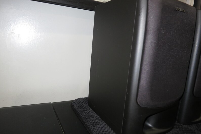 May include: A black Sony bookshelf speaker with a rectangular cabinet and a fabric grille covering the front driver. The speaker features a smooth matte finish on the side panel and a small port opening located at the bottom of the front face.