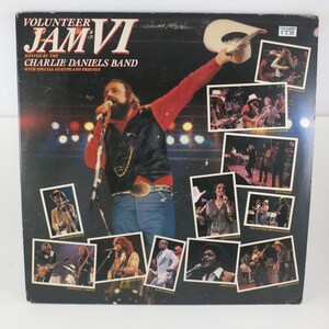 May include: Vintage vinyl record album cover for "Volunteer Jam VI" hosted by The Charlie Daniels Band. The cover features a live performance photo of Charlie Daniels, surrounded by smaller photos of other performers.