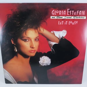 May include: Album cover for "Let It Loose" by Gloria Estefan and Miami Sound Machine. The cover features a woman with dark hair and a black jacket against a red background. The album title and artist name are displayed in white text.