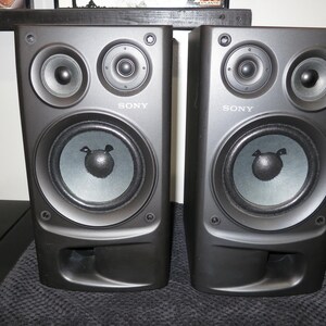 May include: A pair of black Sony bookshelf speakers, each featuring a large woofer, a smaller tweeter, and a rectangular bass reflex port at the bottom. The Sony brand name is printed in white lettering on the front of each speaker cabinet.