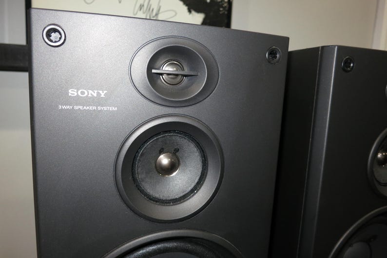 May include: Close-up of two black Sony 3-way speaker systems. The speakers have a matte finish and feature multiple circular speaker components. The Sony logo and "3 WAY SPEAKER SYSTEM" are printed on the front of the speaker.