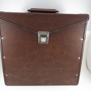 May include: A brown leather briefcase with a silver clasp and handle. The briefcase has a rectangular shape with a flap closure and metal rivets along the edges. The leather has a slightly worn appearance.