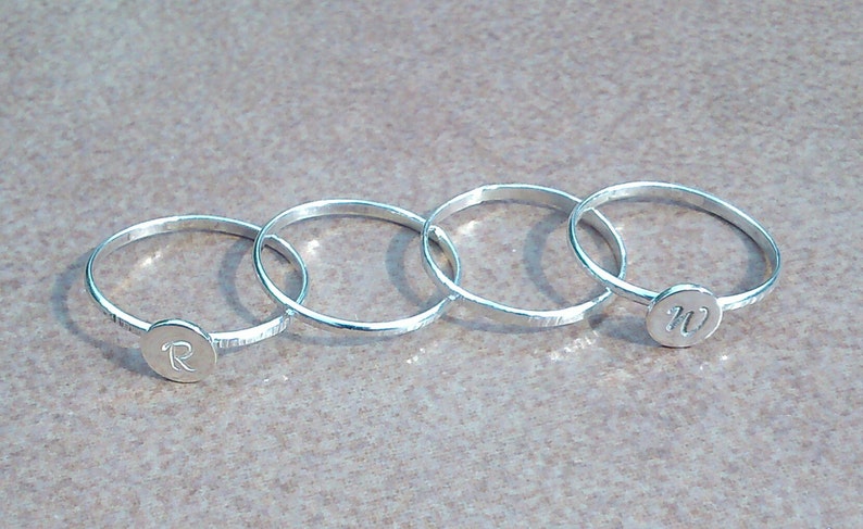 以下が含まれることがあります： 正面に「R」と「M」のイニシャルが刻まれた銀の指輪が4つ。指輪は重ねられています。