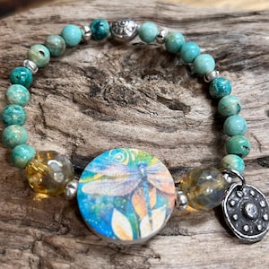 Op de afbeelding: Een set van drie keramische mokken met een gespikkelde, crèmekleurige glazuur. Elke mok heeft een handgeschilderd bloemmotief in blauw, groen en geel. De mokken hebben een eenvoudige, afgeronde vorm en een comfortabel handvat.