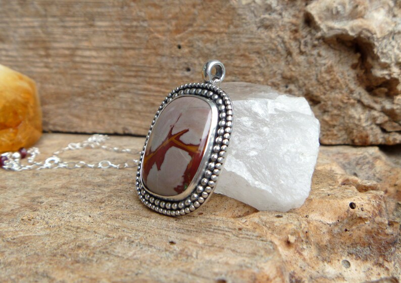 May include: A silver pendant with a brown and red agate stone set in a beaded bezel. The pendant is on a silver chain.