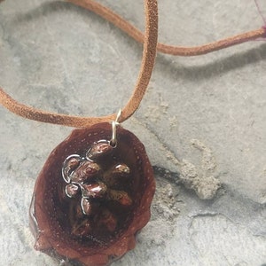 May include: A brown leather cord necklace with a pendant made from a dark brown wood slice with a resin-filled center. The wood slice has a natural, organic shape and the resin is clear and shiny.
